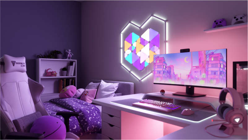This is an image of Nanoleaf Shapes Triangles and Mini Triangles on the wall above the desk and behind the monitor in a gaming battlestation. These RGB lights have over 16 million colors and are perfect for the gamer in your home. The modular smart light panels are connected together with linkers to create a design.