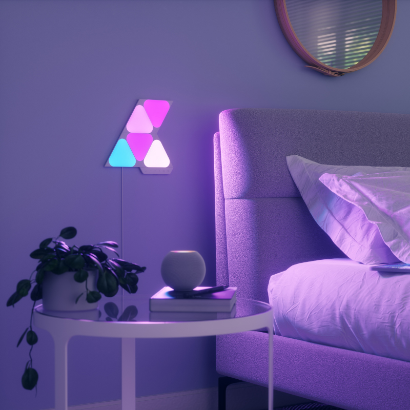Nanoleaf Shapes Thread enabled color changing mini triangle smart modular light panels mounted to a wall in a bedroom. Similar to Philips Hue, Lifx. HomeKit, Google Assistant, Amazon Alexa, IFTTT.